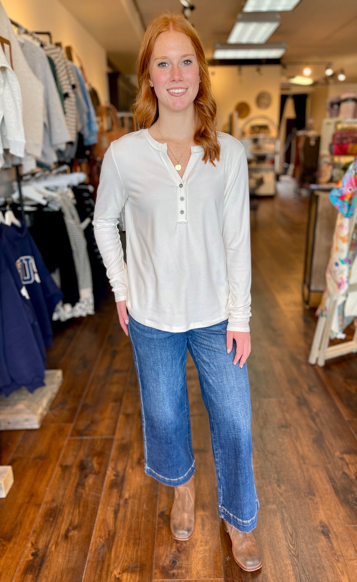 A woman smiling outdoors on a sidewalk, wearing a fitted white long-sleeve henley-style top