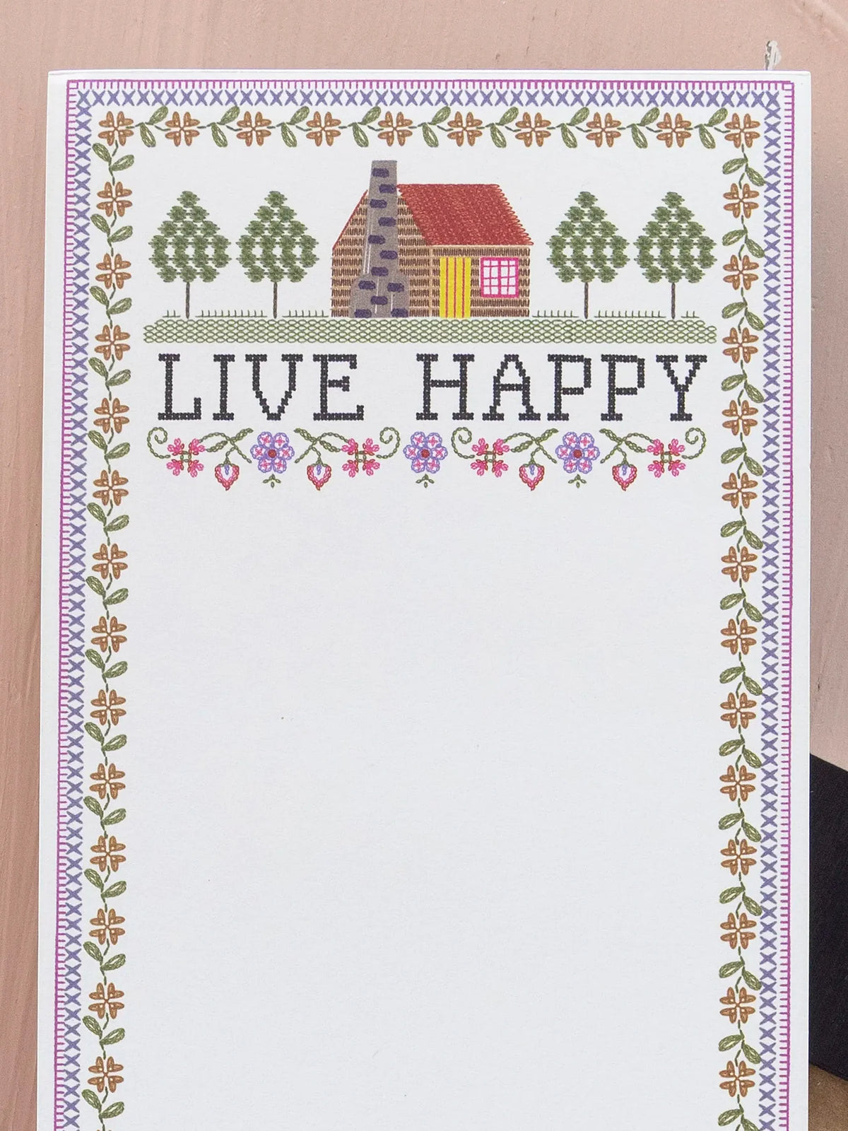 MAGNETIC NOTE PAD THAT SAYS LIVE HAPPY WITH A SMALL COTTAGE ON IT AND A BLUE AND PINK BACKGROUND.