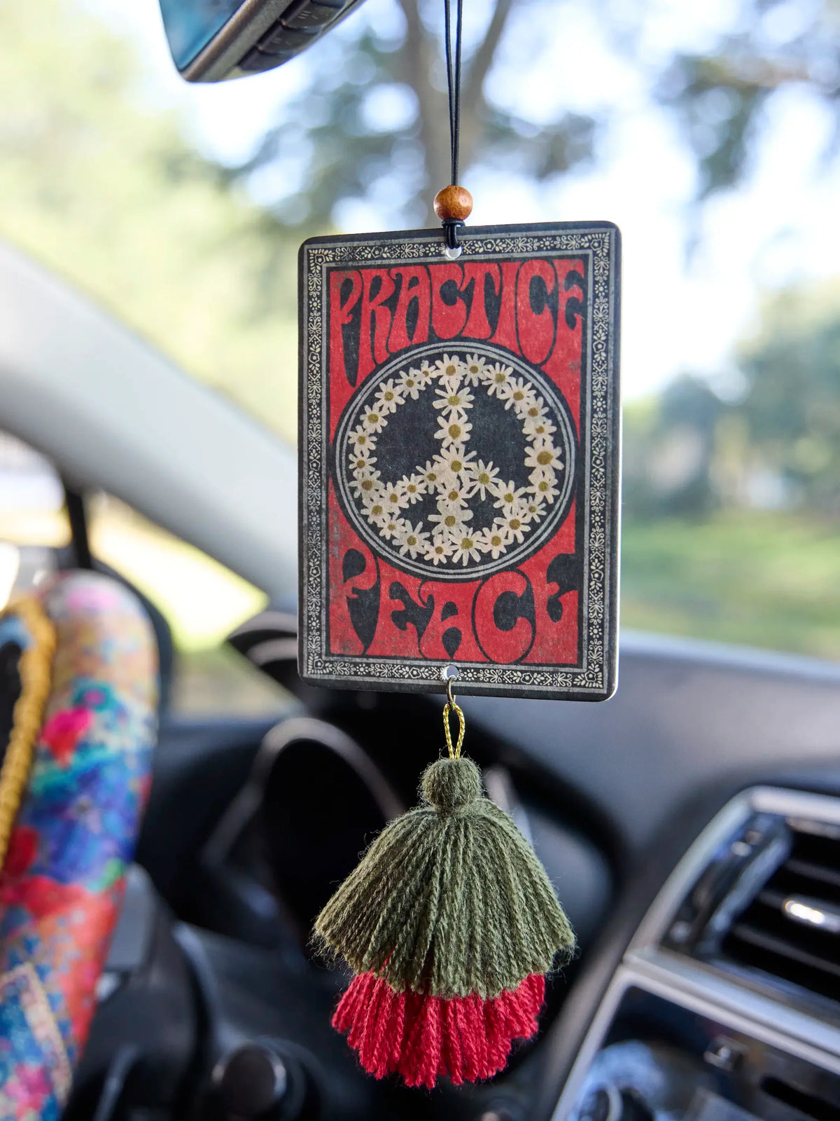 AIR FRESHENER WITH THE WORDS PRACTICE PEACE HANGING FROM REAR VIEW MIRROR