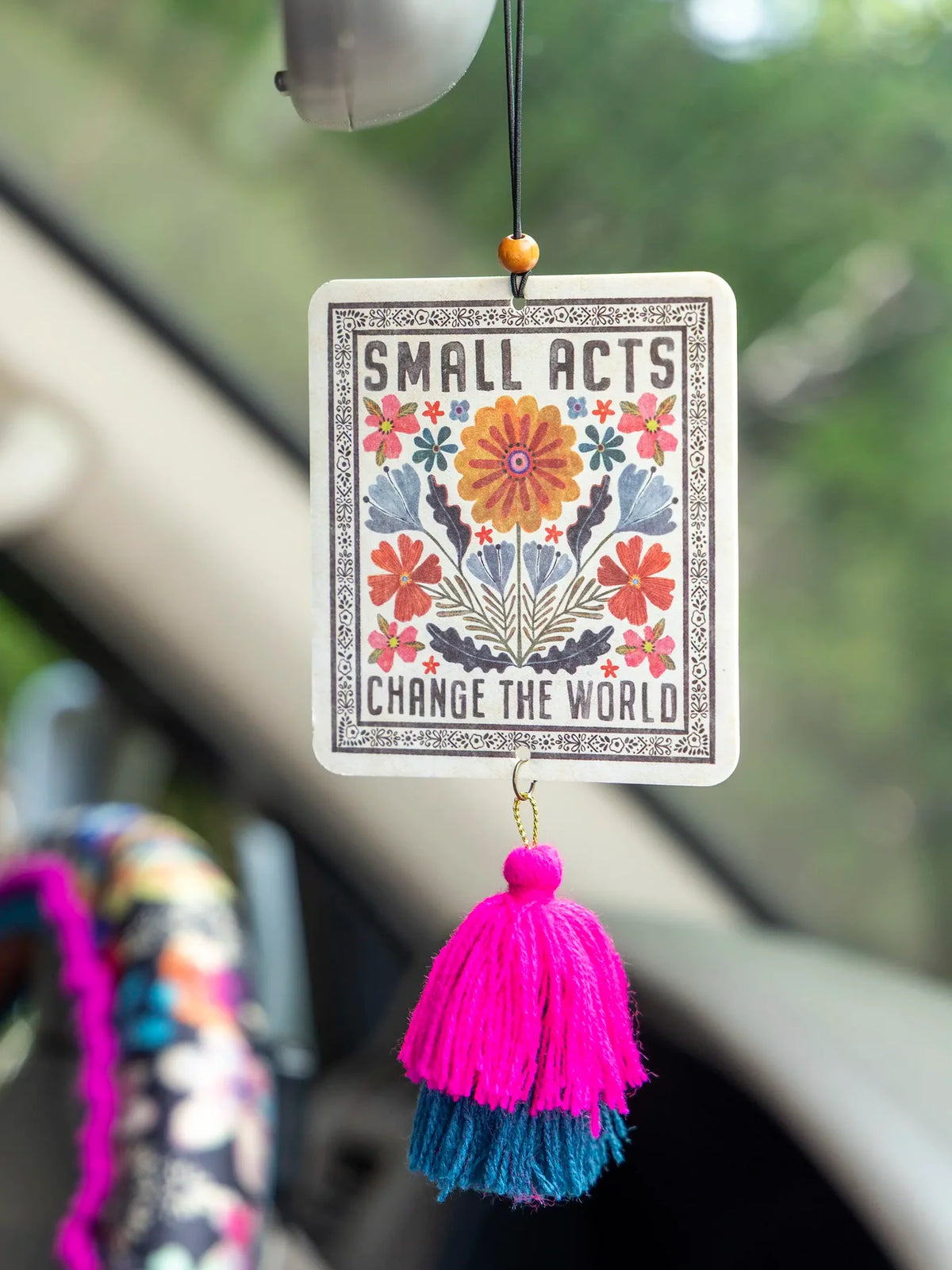 SQUARE AIR FRESHENER WITH FLOWERS BLUE AND PINK TASSLES AND THE WORDS SMALL ACTS CHANGE THE WORLD