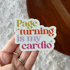Hand holding a colorful sticker with text 'Page turning is my cardio' against a textured white background.