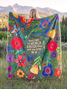 WOMAN HOLDING MULTI COLOR BLANKET WITH FLOWERS AND THE WORDS YOU MAKE THE WORLD A BETTER PLACE JUST BY BEING IN IT