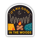 An arched sticker featuring a camping scene with the text 'IT'S ALL GOOD IN THE WOODS'. The design shows pine trees, a crescent moon, stars, a campfire, a tent, logs, and a body of water on a dark background with a white border.
