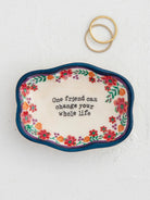 DECORATIVE BOWL WITH ONE FRIEND CAN CHANGE YOUR WHOLE LIFE WITH FLOWERS AND NAVY RIM 2 RINGS SET TO THE SIDE ON A WHITE BACKGROUND
